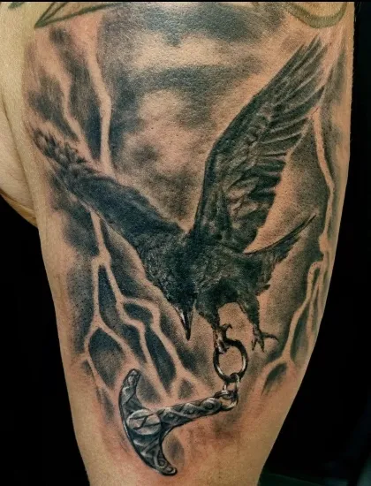 Raben-Tattoo mit Thors Hammer: Hugin oder Munun mit Mjölnir und dynamischen Hintergrund der ein Gewitter symbolisiert auf einem Oberarm. Tattoo in Hamburg von Ozzy gestochen