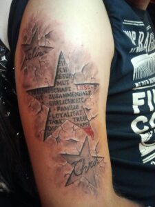 Rot-schwarzes Stern-Tattoo mit Schrift über Familie und Werte auf dem Oberarm, das wie eingeritzt aussieht. Tattoo in Hamburg von Ozzy gestochen