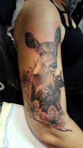 Ein detailliertes Tattoo eines Rehs mit Blumenmotiven auf einem Arm . Tattoo in Hamburg von Ozzy gestochen