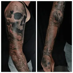Detailreiche Tattoos eines großen Schädels und vielen kleinen als Teil der Pariser Katakomben als Sleeve auf dem Arm. Tattoo in Hamburg von Ozzy gestochen