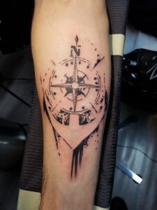 Ein Anker, der in einen Kompass übergeht, als Tattoo im Trash-Polka-Stil. Anker-Tattoo von Ozzy in Hamburg gestochen.