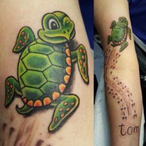 Eine grüne Cartoon-Schildkröte auf dem Arm, die eine Sandspur hinterlässt, die zum Namen Tom führt. Schildkröten-Tattoo von Ozzy in Hamburg gestochen.