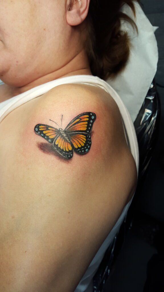 Ein farbenfroher Monarchfalter mit 3D-Effekt als Tattoo auf der Schulter. Schmetterling-3D-Tattoo von Ozzy in Hamburg gestochen.