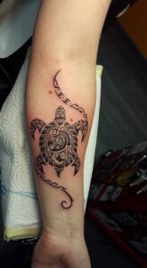 Eine Schildkröte, verziert mit polynesischen Mustern und umgeben von Ranken, auf dem Unterarm. Schildkröten-Tattoo von Ozzy in Hamburg gestochen.