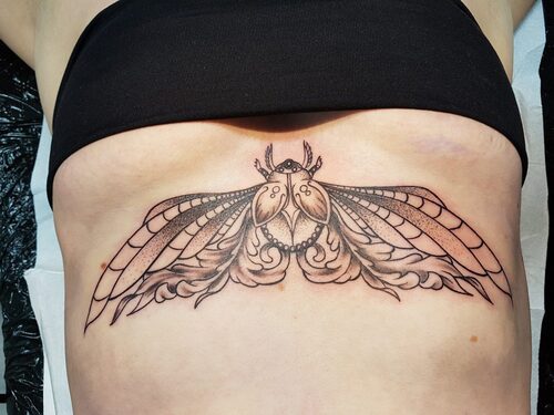 Ein großer Skarabäus-Käfer mit verzierten Flügeln als Black and Grey Underboob-Tattoo. Skarabäus-Tattoo von Ozzy in Hamburg gestochen.